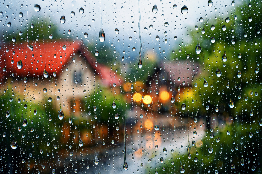 Raindrops on window with blurred village houses and lights behind